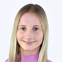 Eine junge Frau mit langen blonden Haaren und blauen Augen lächelt in Richtung Betrachter. 