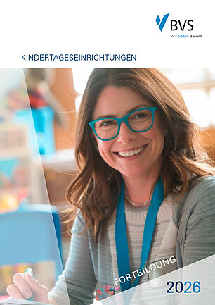 BVS Fortbildung 2026 - Cover KiTa Eine Frau mit einem weißgrauen geringelten Pullover trägt eine türkisfarbenen Brille und hat lange dunkelblonde Haare. Sie sitzt lächelnd an einem Tisch in einer Kita.