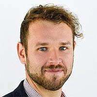 Ein junger Mann mit hellbraunem lockigen gewellten Haar und einem Vollbart.