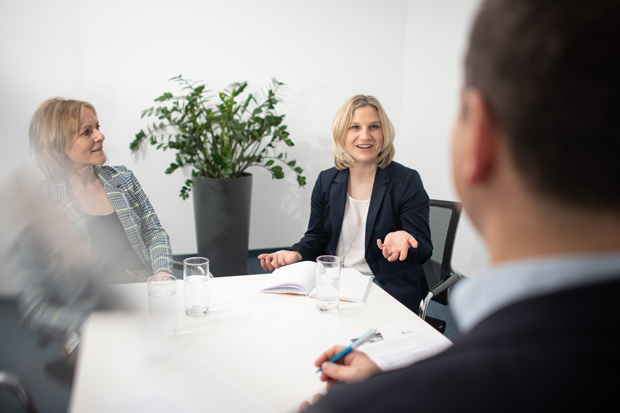 Themenbild Neu im Personalbereich An einem weißen Tisch auf dem Gläser stehen sitzen 3 Personen.