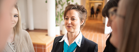 Themenbild Unsere Kunden In der Mitte einer kleinen Gruppe sieht man eine Frau mit kurzen Haaren einer weißen Bluse mit BVS Logo und einem dunkelblauen Blazer.