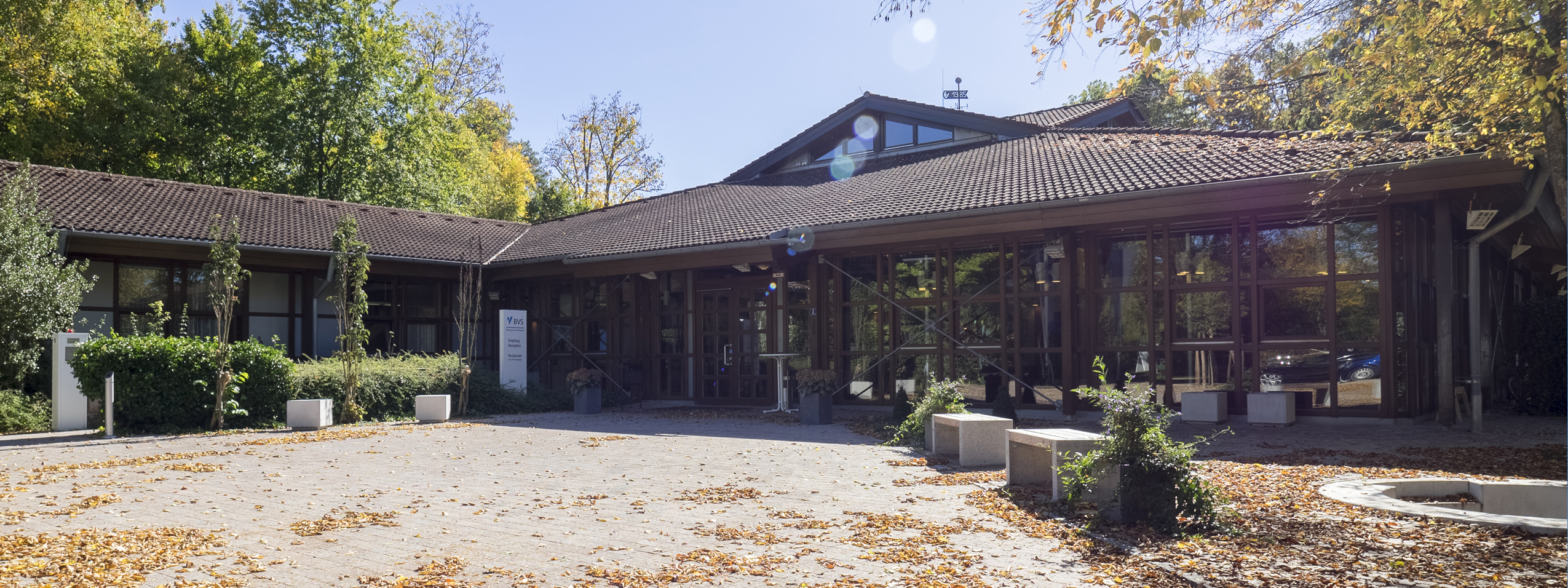 Das Bild zeigt den aus dunklem Holz bestehenden Eingangsbereich des Bildungszentrums Holzhausen im Herbst vor blauem Himmel